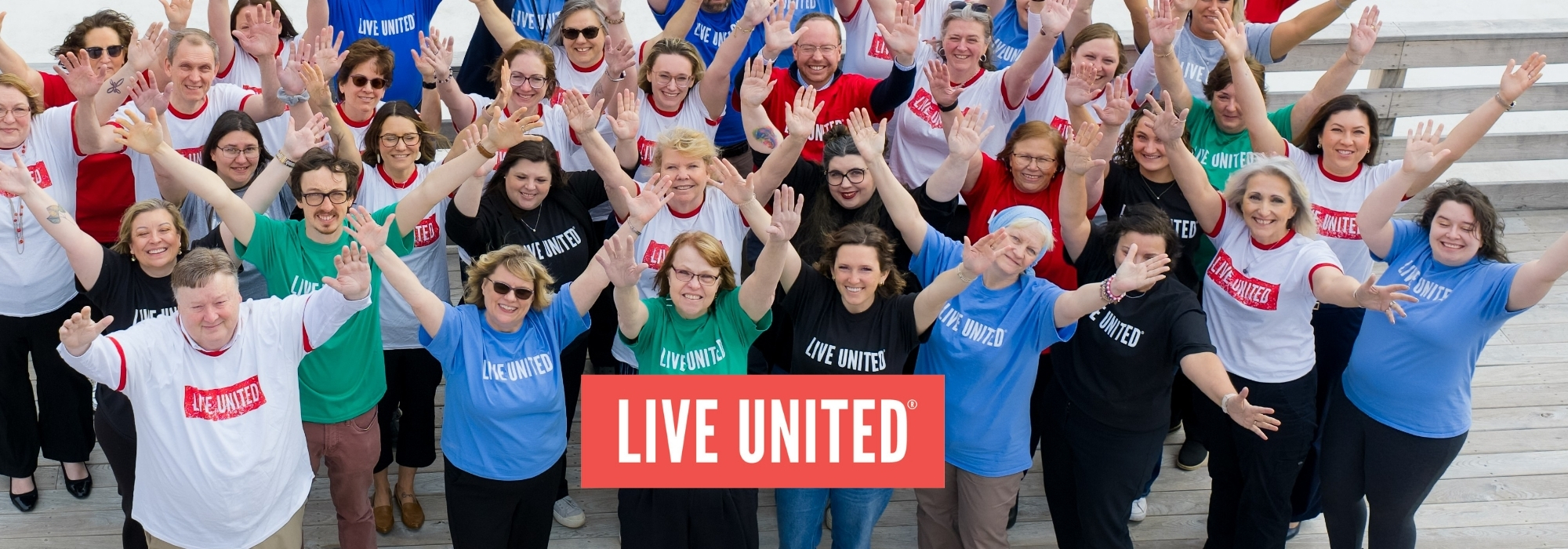 Large group wearing LIVE UNITED shirts with hands in the air
